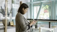 ai-untuk-customer-service-balas-chat Perempuan berjas kotak-kotak mengetik di ponsel di meja kafe