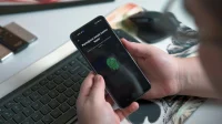 Tangan memegang ponsel yang menampilkan layar pendaftaran sidik jari di dekat keyboard