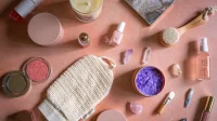 Aneka produk perawatan kulit dan kosmetik seperti botol serum, wadah krim, dan kuas di atas meja merah muda