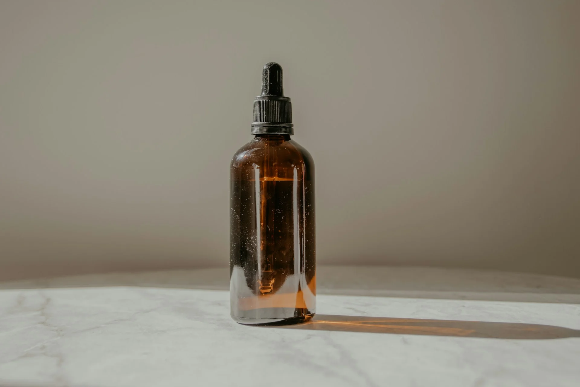 Botol kaca amber berpipet hitam tanpa label berdiri di atas meja marmer