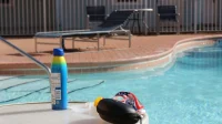 Botol semprot sunscreen biru di tepi kolam renang, ilustrasi cara memilih sunscreen