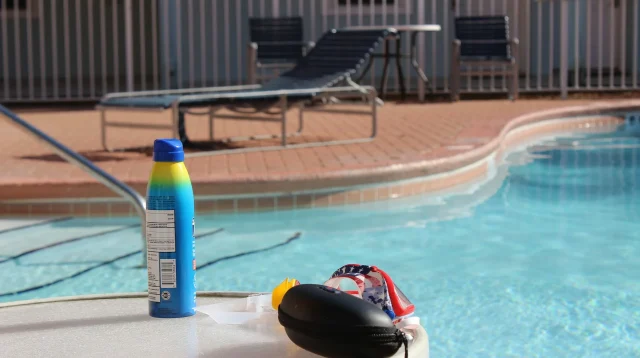 Botol semprot sunscreen biru di tepi kolam renang, ilustrasi cara memilih sunscreen