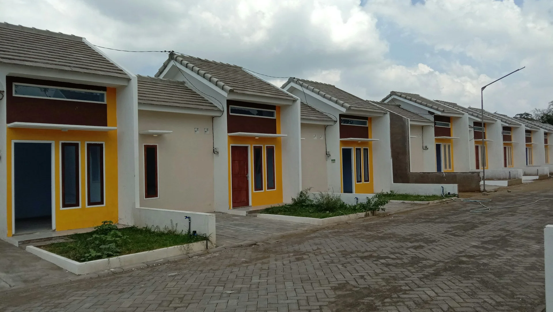 Deretan rumah tapak sederhana satu lantai dengan pintu kuning dan merah di kompleks perumahan baru