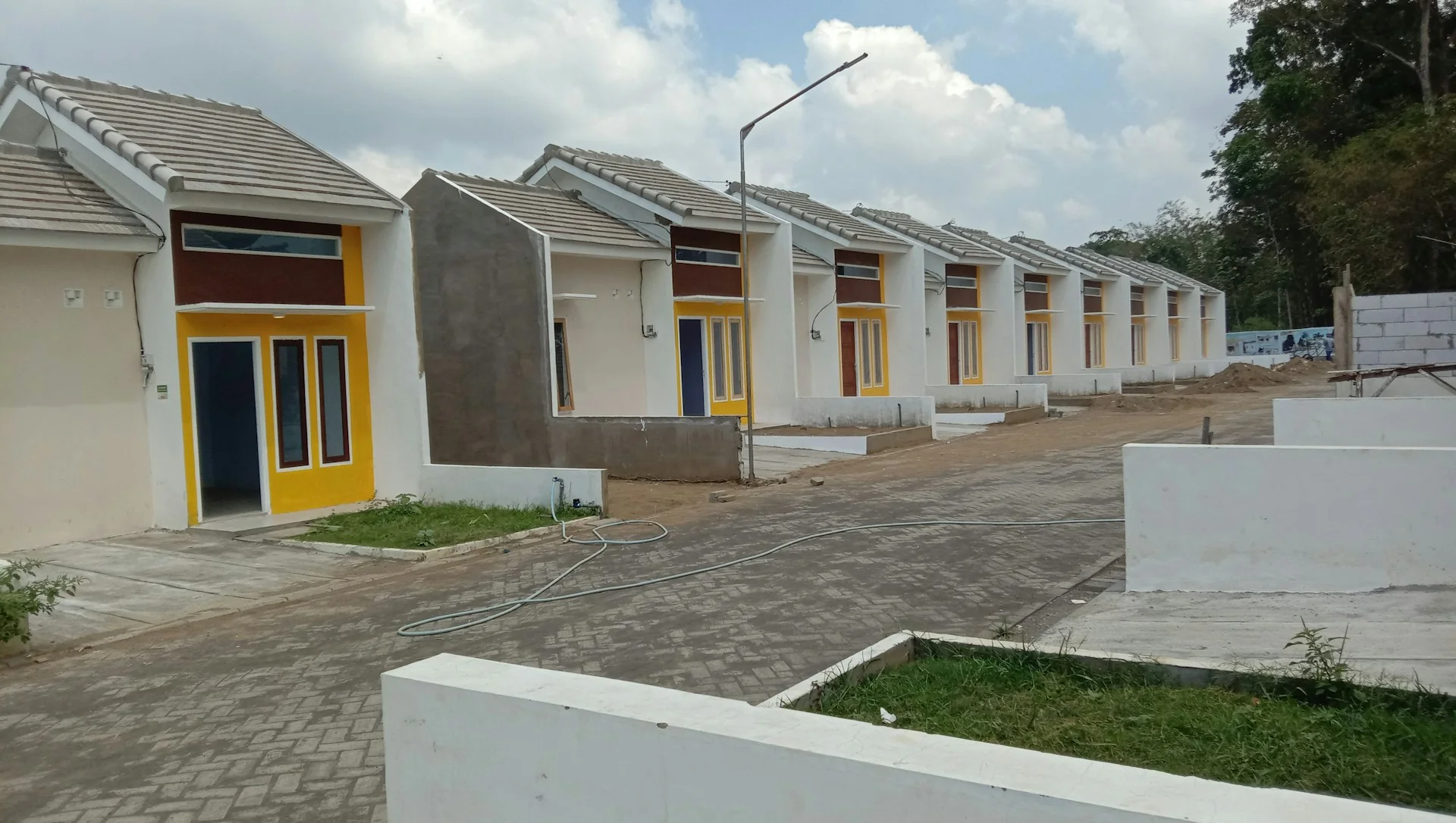 Deretan rumah tapak satu lantai dengan pintu kuning di kompleks perumahan baru berjalan paving