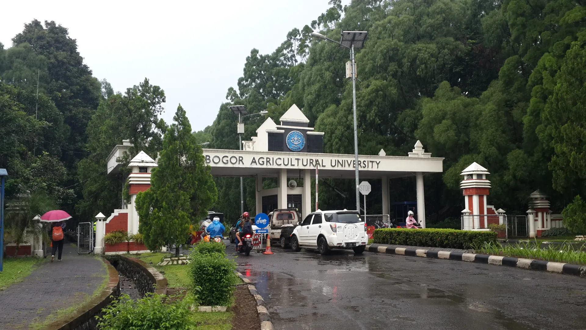 Gerbang utama kampus IPB Dramaga Bogor saat hujan dengan kendaraan melintas