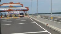 Gerbang Tol Benoa di Tol Bali Mandara dengan atap ornamen Bali, papan lajur khusus transaksi elektronik, dan sebuah bus yang melintas