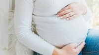 Ibu hamil bersweter putih memegang perutnya dengan kedua tangan
