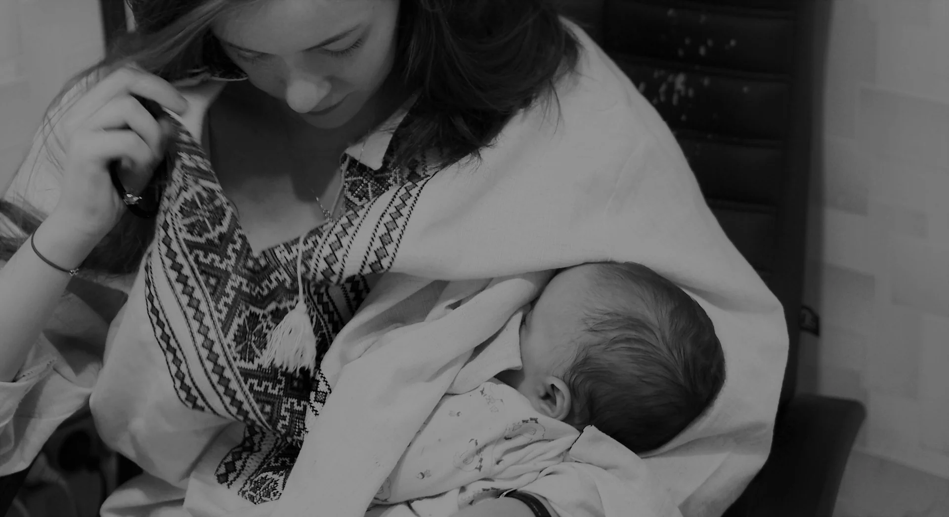 Foto hitam putih seorang ibu menyusui bayi dalam gendongan sambil menunduk