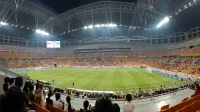 Interior Jakarta International Stadium saat pertandingan sepak bola malam hari dengan penonton di tribun
