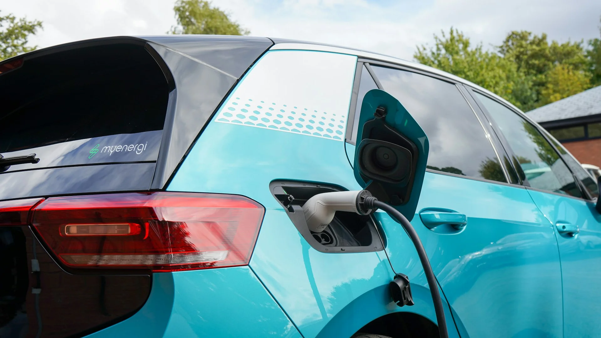 Konektor charger terpasang di port pengisian daya mobil listrik hatchback berwarna biru toska