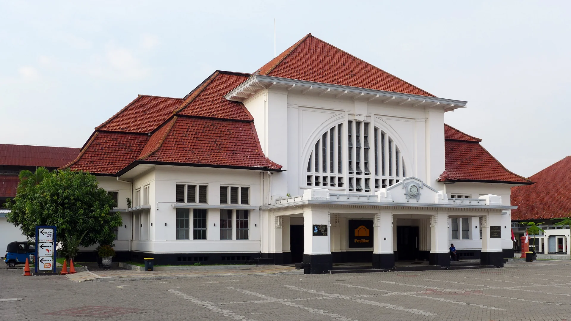 Gedung Kantor Pos Surabaya bergaya kolonial dengan atap genteng merah dan logo Pos Indonesia di pintu masuk