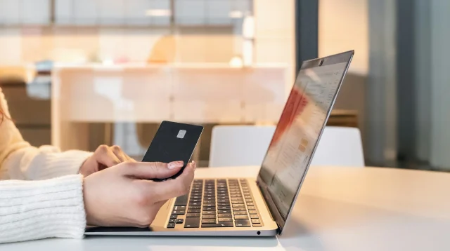 Tangan memegang kartu pembayaran di depan laptop saat belanja online