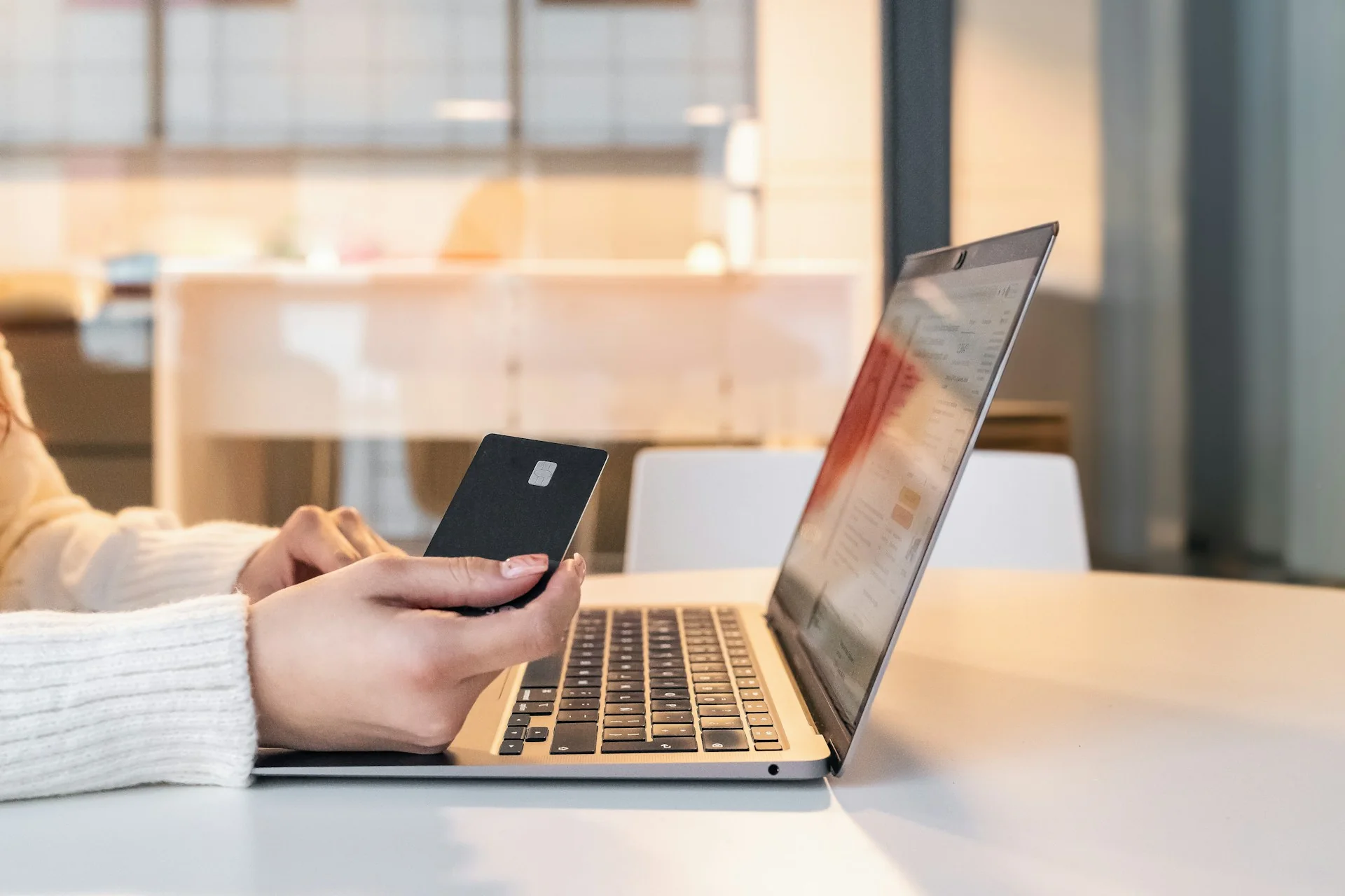 Tangan memegang kartu pembayaran di depan laptop saat belanja online