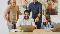 kolaborasi-digital-tim-kecil-laptop Empat rekan kerja berdiskusi di depan satu laptop di meja kantor