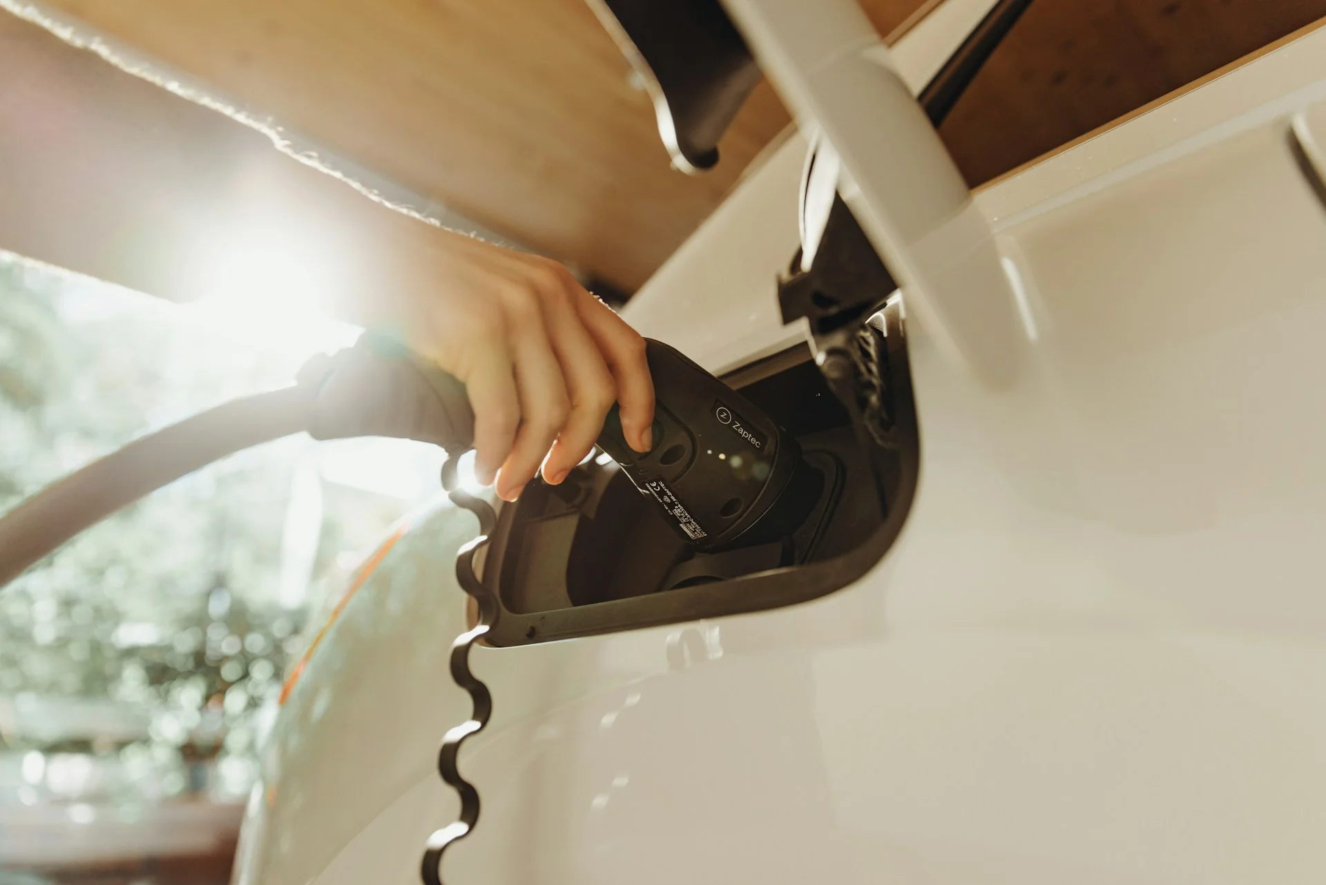 Tangan mencolokkan konektor charging Type 2 ke port pengisian daya mobil listrik putih