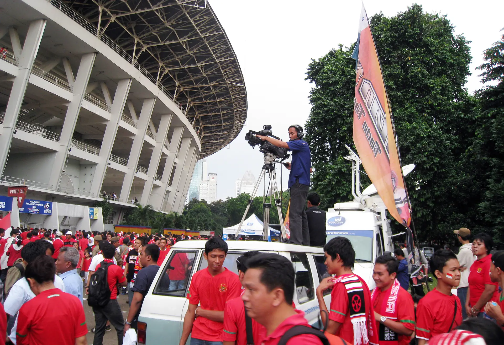 Juru kamera televisi berdiri di atas mobil merekam suasana suporter berbaju merah di luar Stadion Gelora Bung Karno