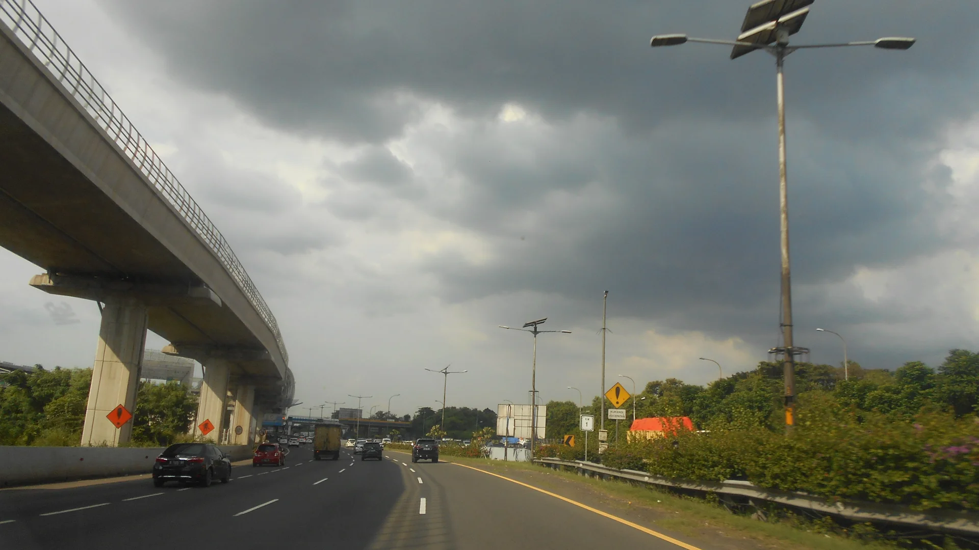 Mobil dan truk melaju di Tol Jakarta-Cikampek di samping tiang Jalan Layang Mohamed bin Zayed saat langit mendung