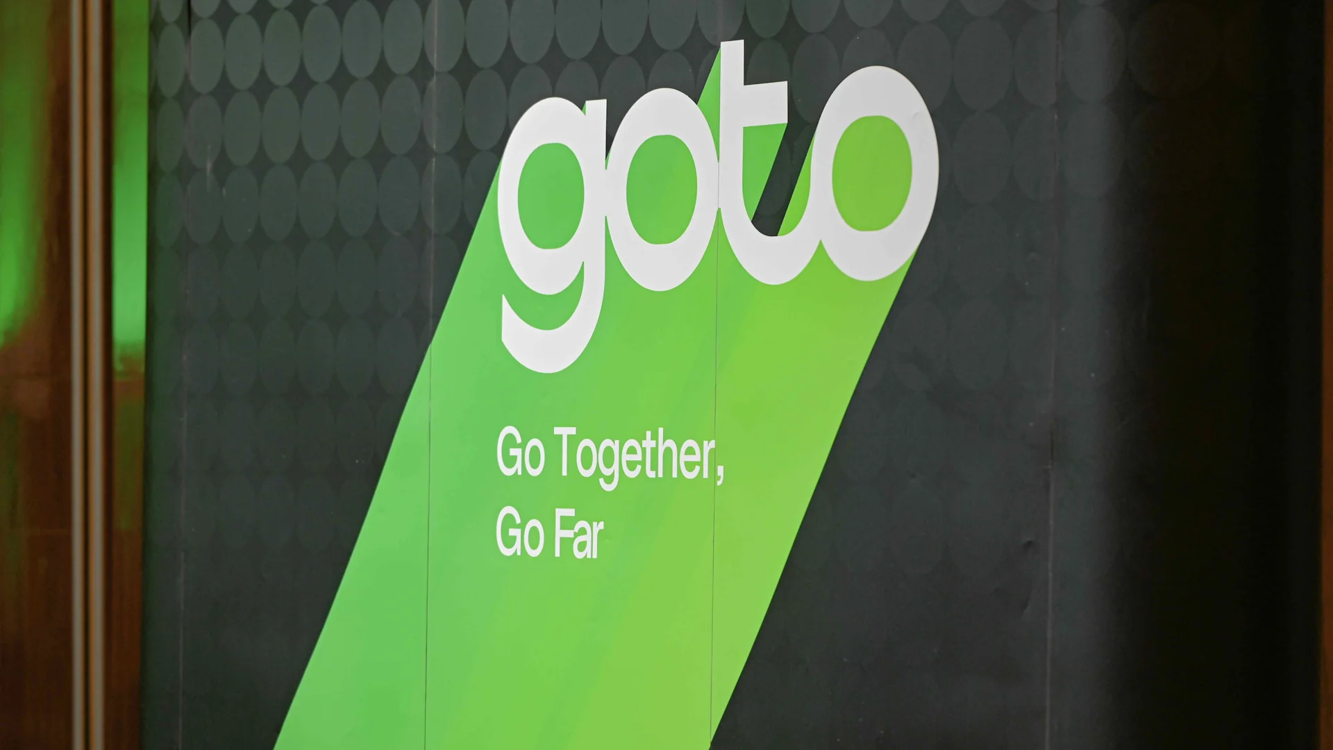 Logo GoTo putih dengan slogan Go Together, Go Far di atas latar hijau dan hitam