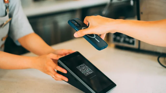Pembeli memegang ponsel untuk memindai kode QR di layar perangkat kasir di meja kedai