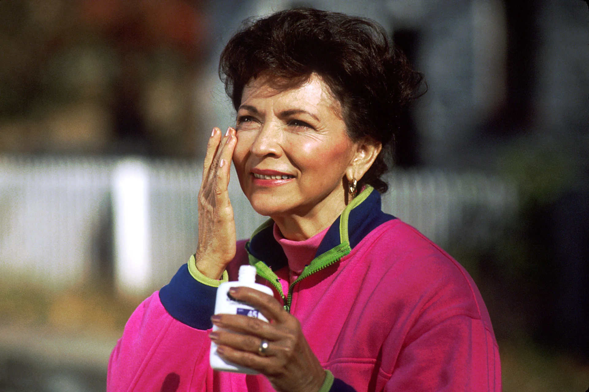 Perempuan mengoleskan sunscreen ke pipi sambil memegang botol SPF 45