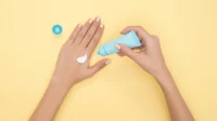 Tangan memencet tube krim pelembap dan mengoleskannya ke punggung tangan di latar kuning
