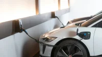 Mobil listrik bekas berwarna putih sedang mengisi daya dari wallbox di parkiran dalam ruangan