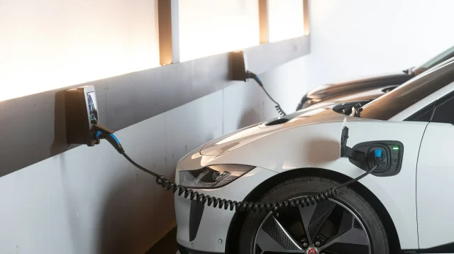 Mobil listrik bekas berwarna putih sedang mengisi daya dari wallbox di parkiran dalam ruangan