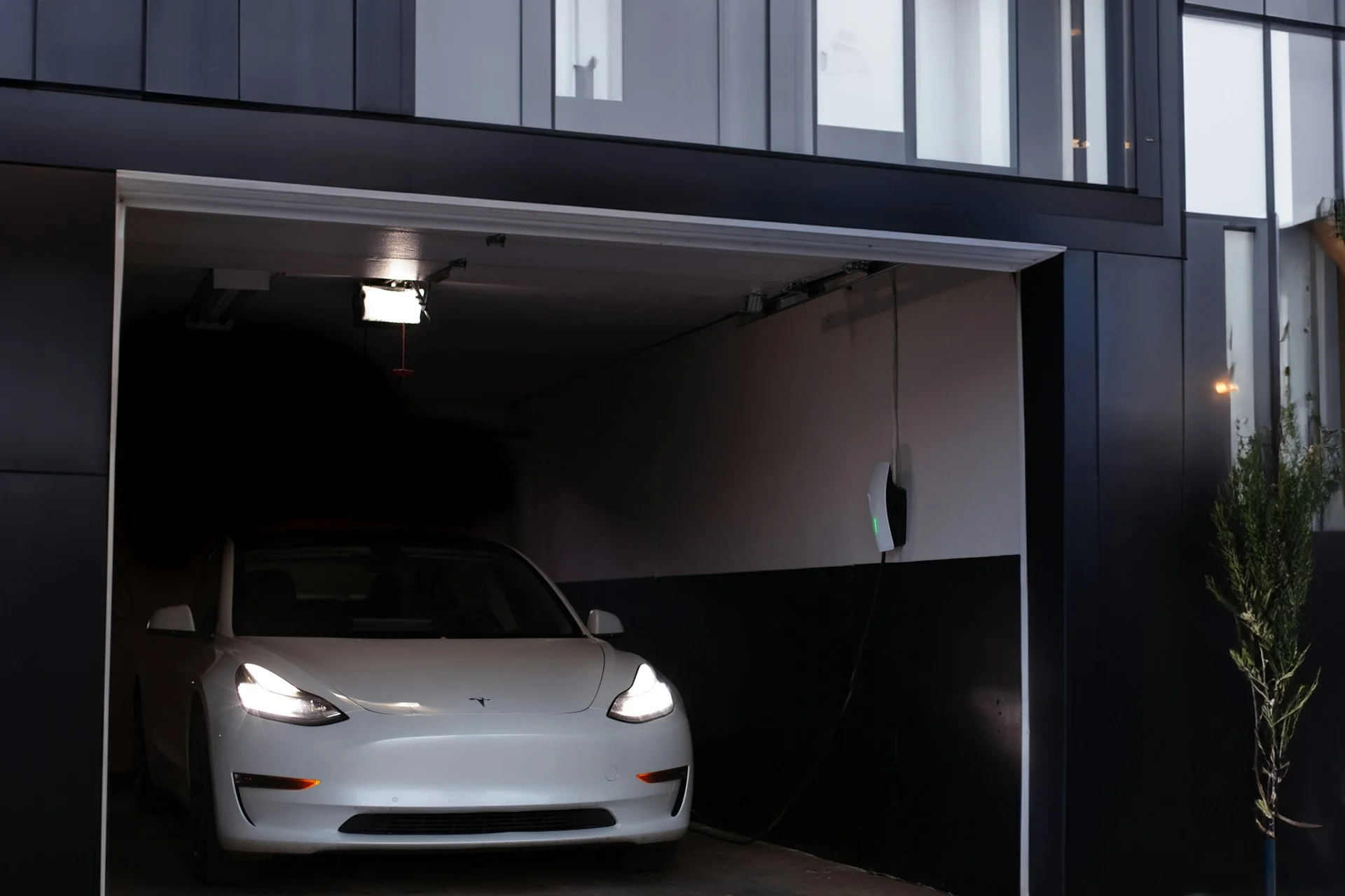 Mobil listrik putih terparkir di garasi rumah, dengan wall charger terpasang di dinding