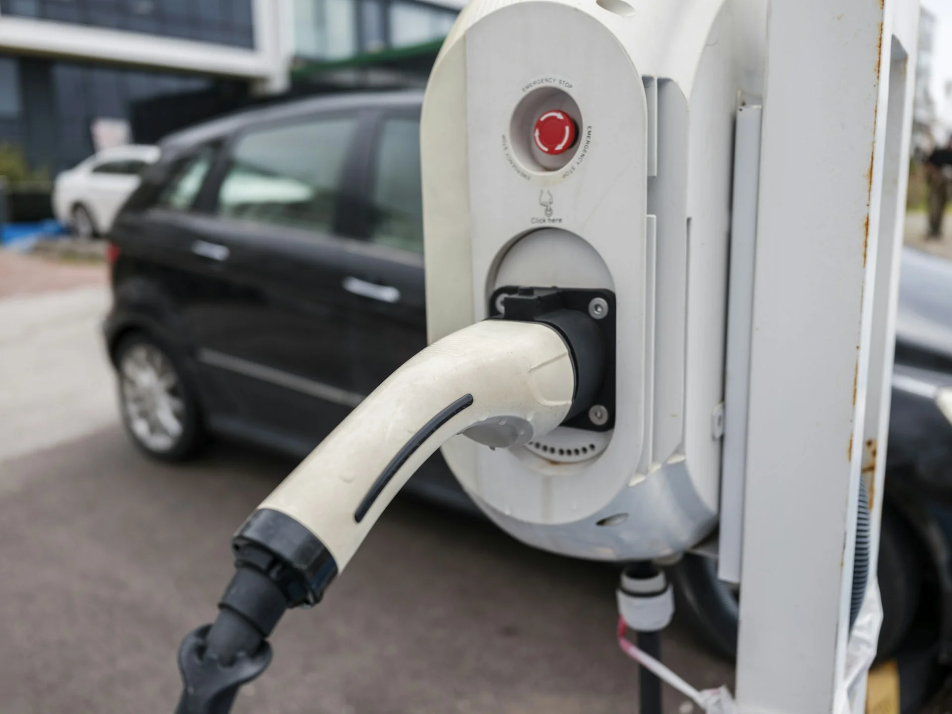 Konektor pengisian daya di unit charger umum dengan mobil terparkir di belakangnya
