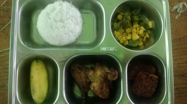 Ompreng baja tahan karat berisi nasi, tumis jagung dan sayur, ayam goreng, tempe, dan pisang menu Makan Bergizi Gratis