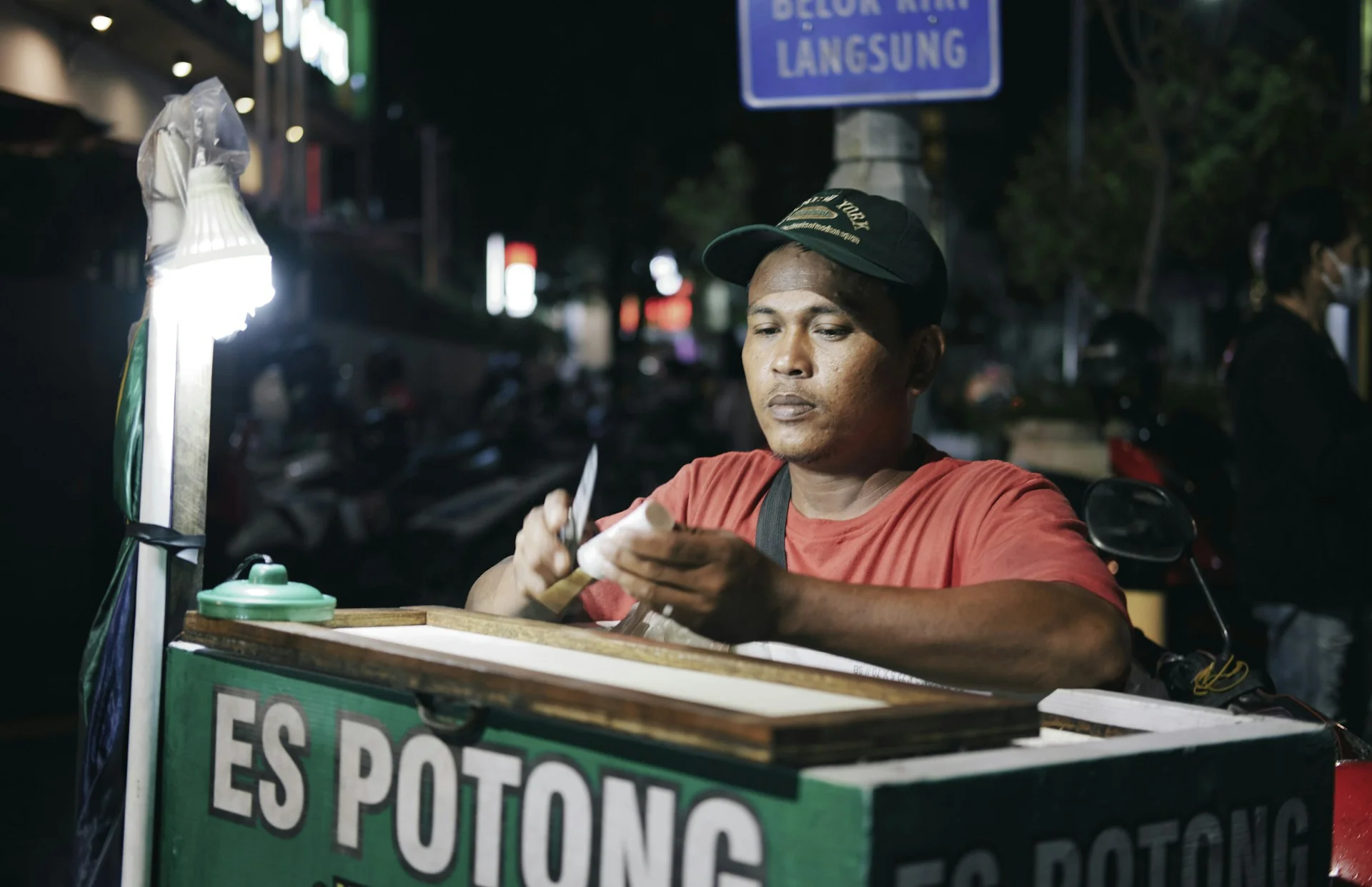 Pedagang es potong berkaus merah melayani di gerobak hijau pada malam hari di Surakarta