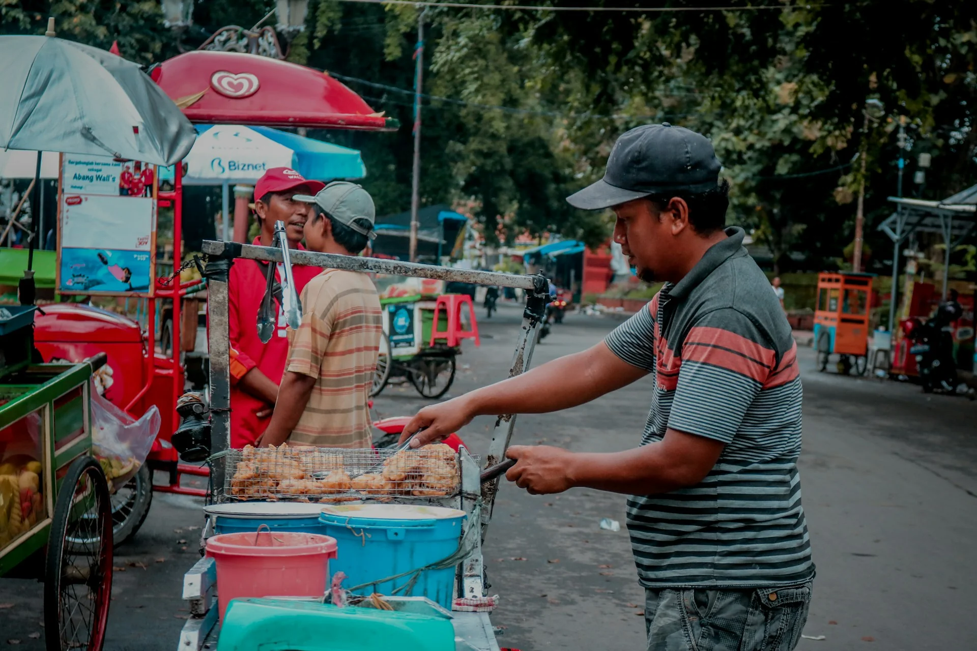 Pedagang kaki lima menggoreng jajanan di gerobak pinggir jalan dengan deretan gerobak lain di belakangnya
