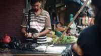 Pedagang di lapak pasar menghitung uang tunai di balik meja dagangan