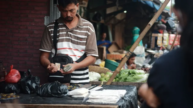 Pedagang di lapak pasar menghitung uang tunai di balik meja dagangan