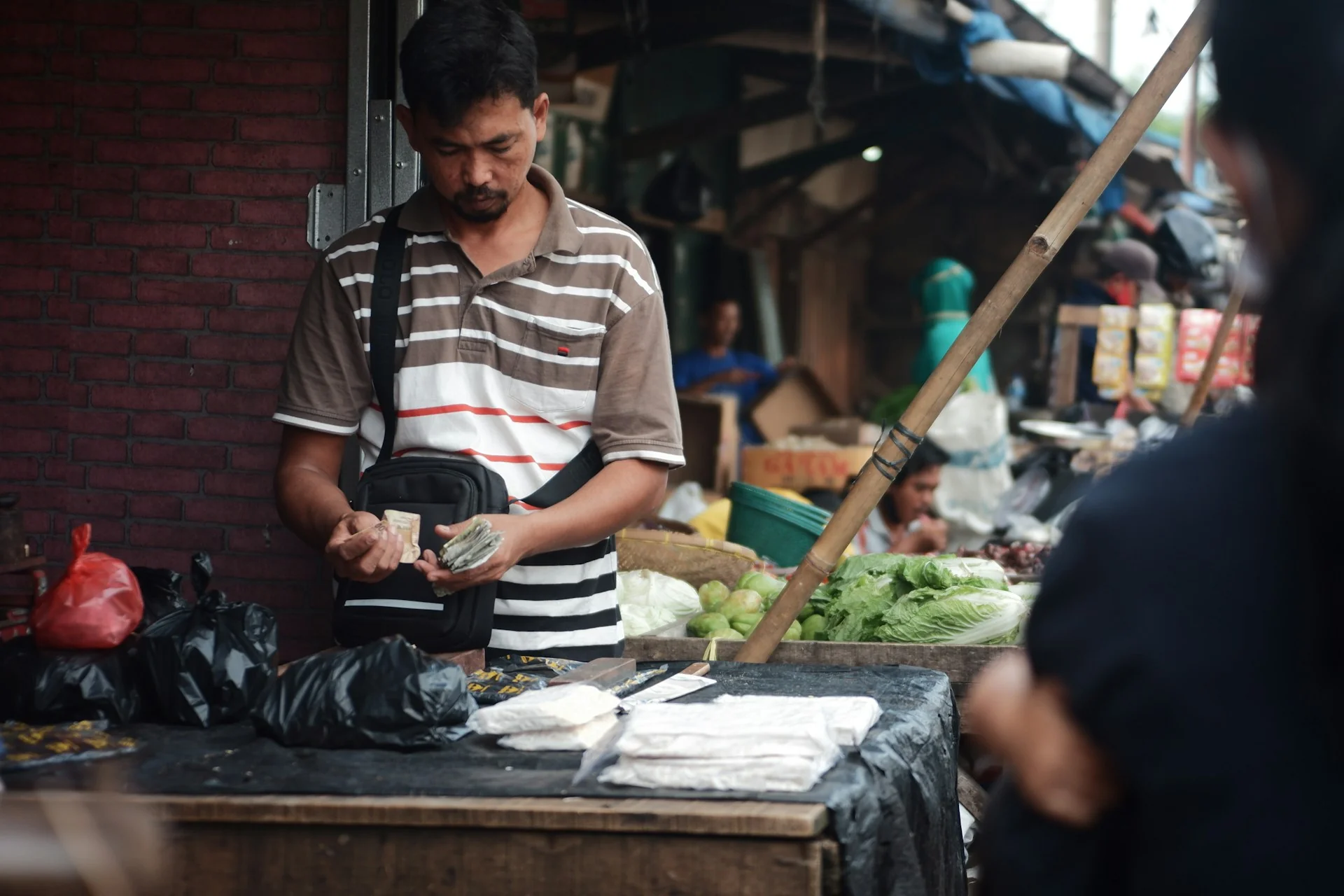 Pedagang di lapak pasar menghitung uang tunai di balik meja dagangan
