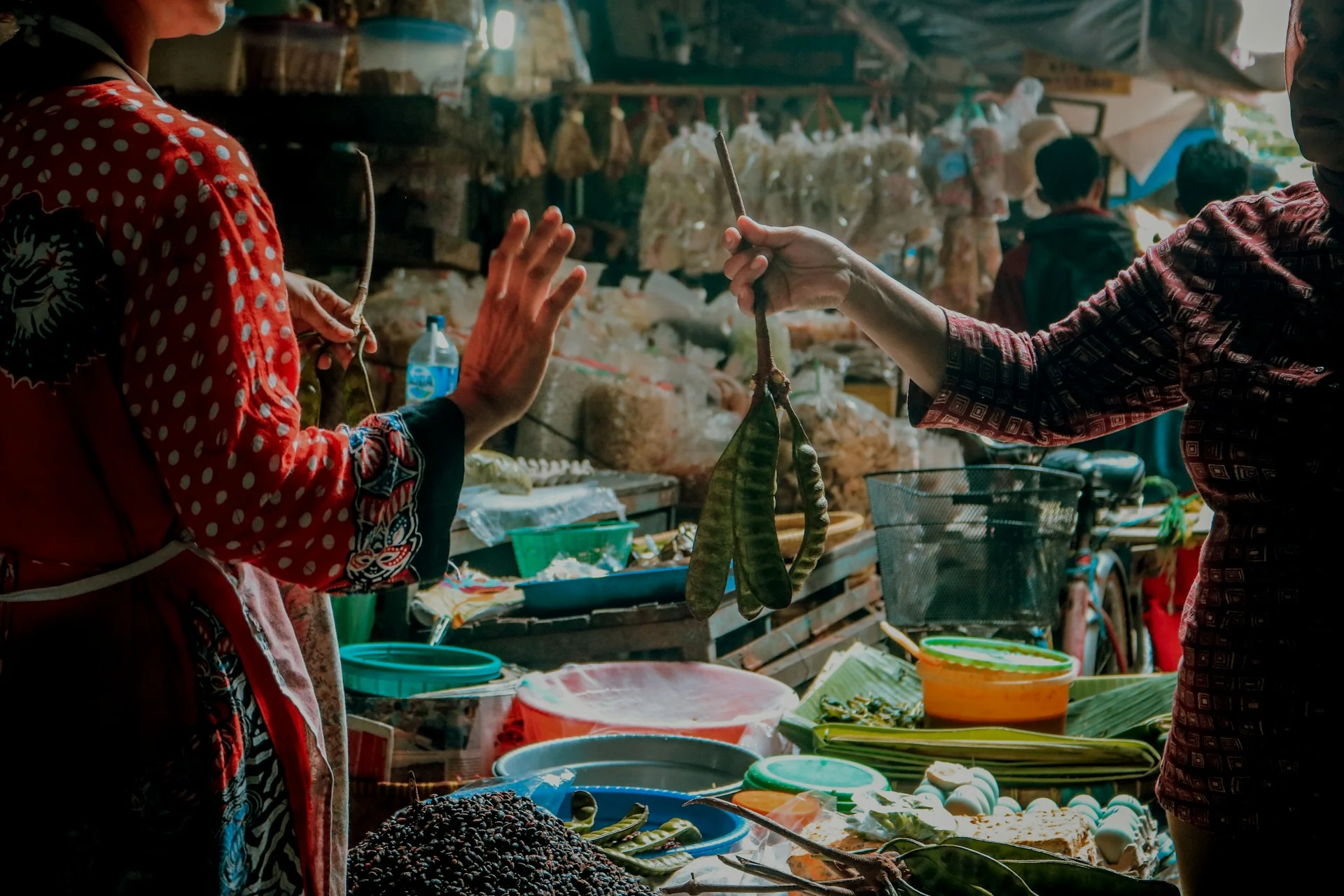 Pedagang pasar tradisional menyerahkan seikat petai kepada pembeli di lapak sayur