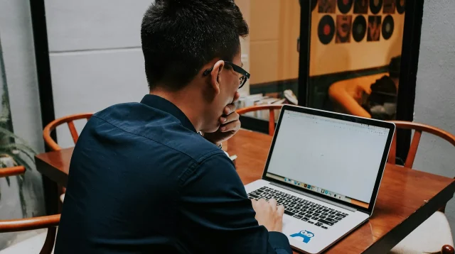 Pekerja lepas bekerja dengan laptop di kafe Pria berkacamata bekerja dengan laptop di meja kayu sebuah kafe