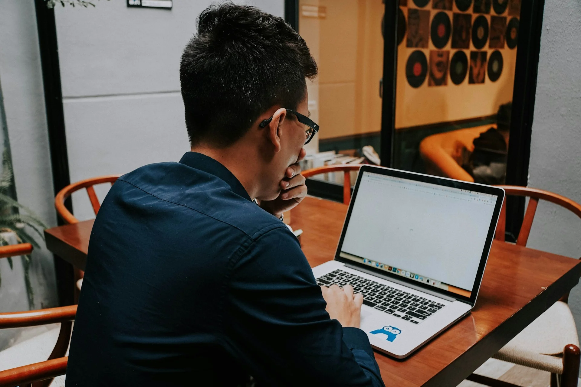 Pria berkacamata bekerja dengan laptop di meja kayu sebuah kafe