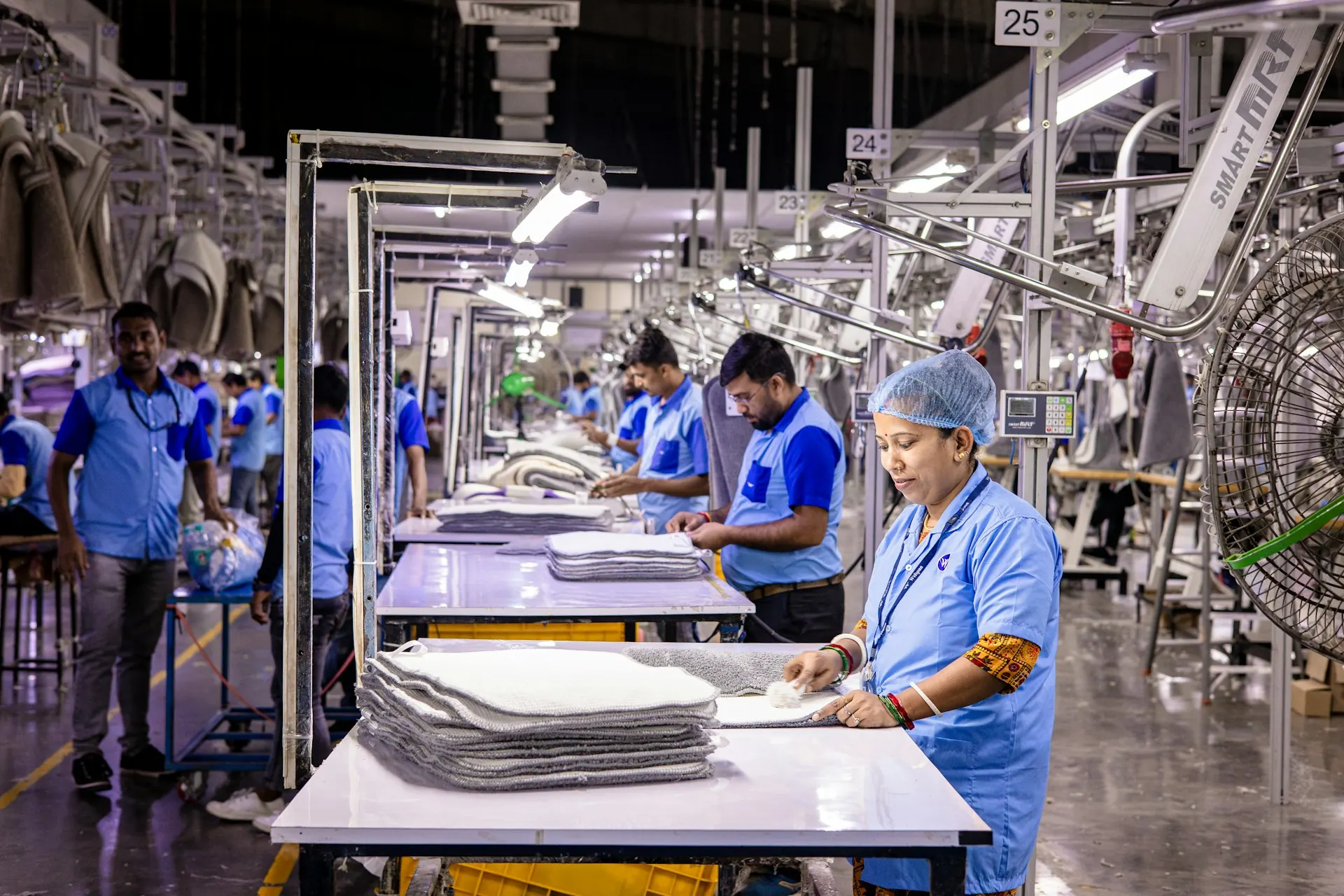 Pekerja berseragam biru menyusun kain di meja lini produksi pabrik garmen