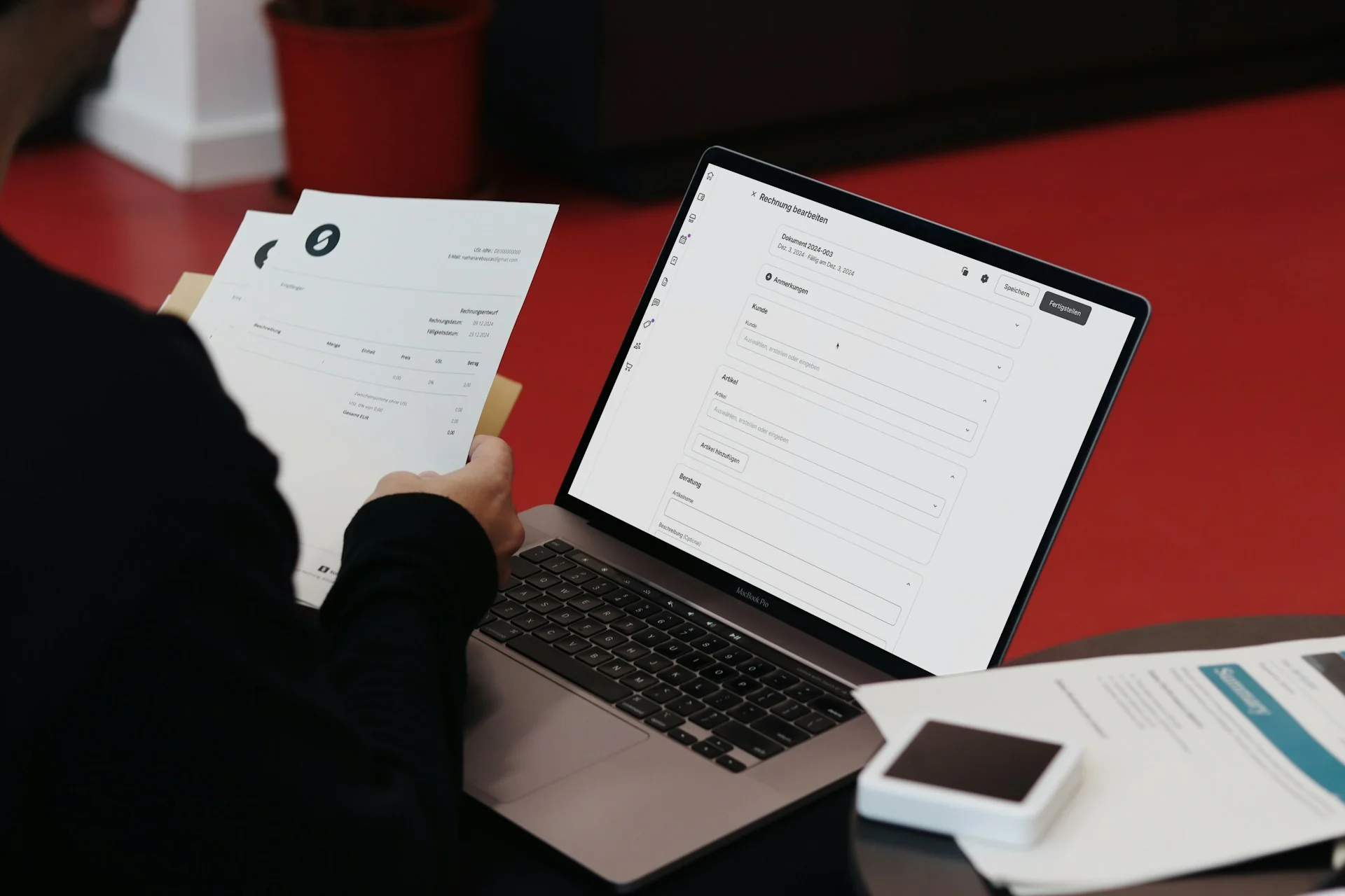 Pekerja memegang lembar dokumen sambil mencocokkannya dengan formulir di layar laptop