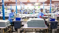 Pekerja berseragam biru menjahit kain di deretan mesin jahit pabrik tekstil