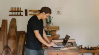 Pemilik usaha kerajinan kayu mengetik di laptop di atas meja kerja bengkelnya