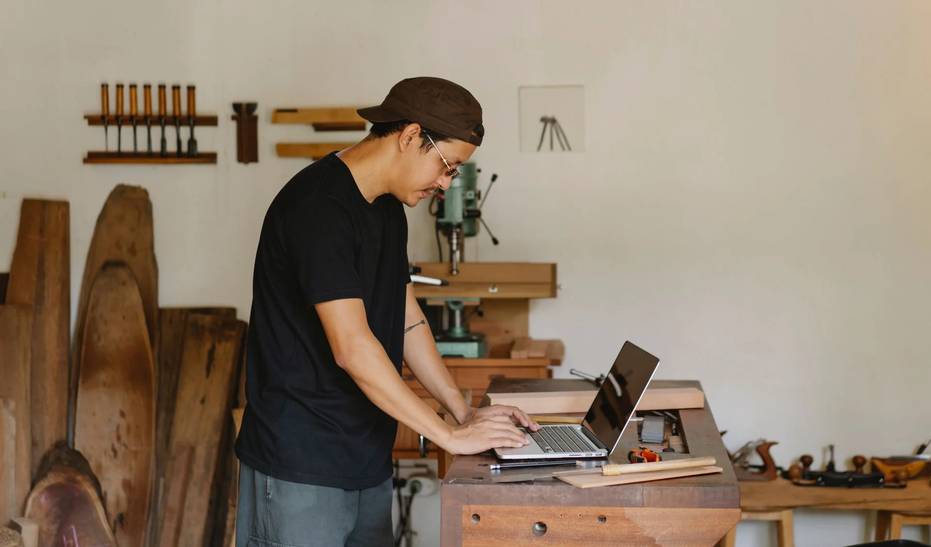 Pemilik usaha kerajinan kayu mengetik di laptop di atas meja kerja bengkelnya