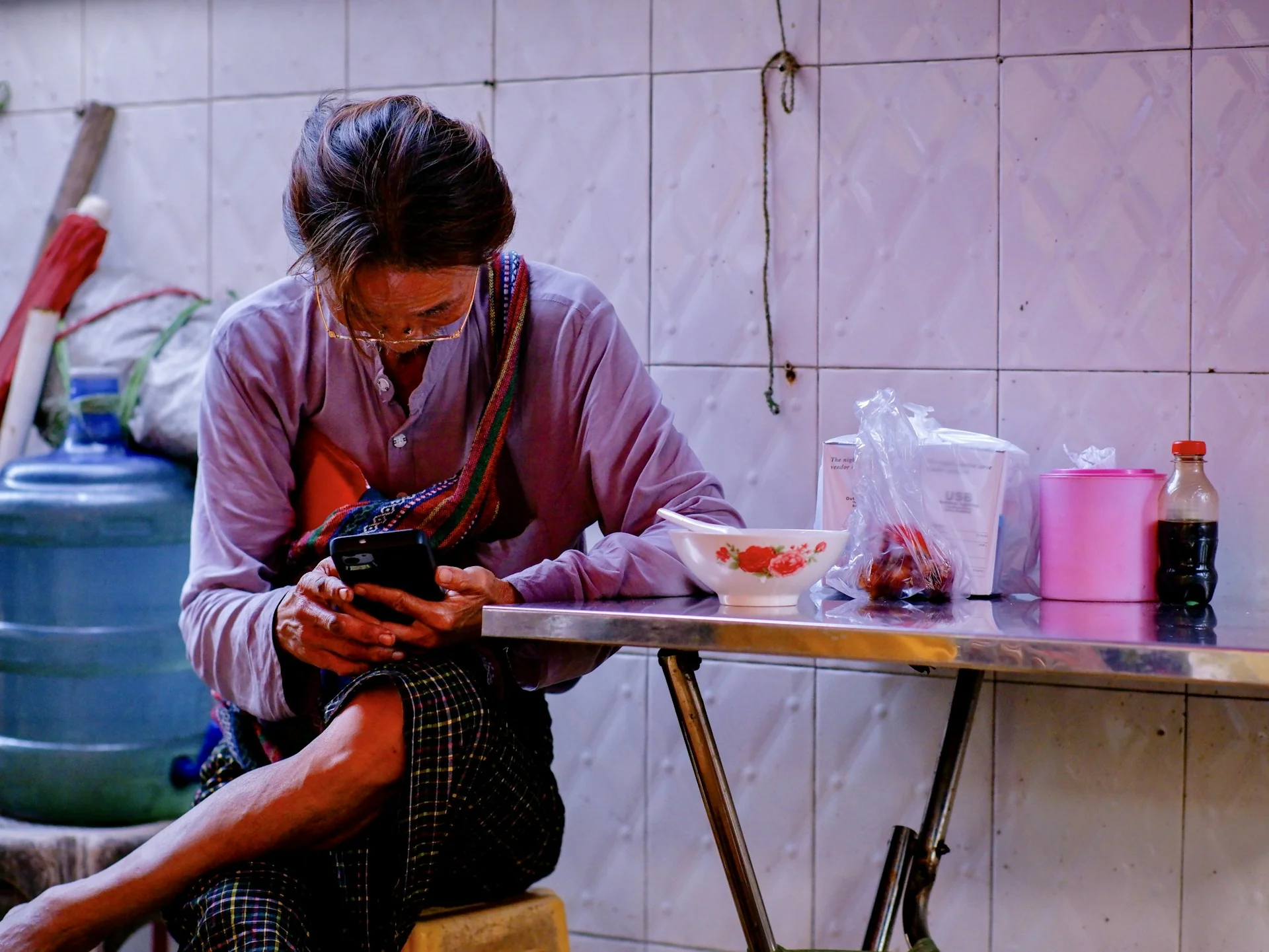 Orang berkacamata duduk di kedai makan sederhana sambil memeriksa ponsel di dekat meja