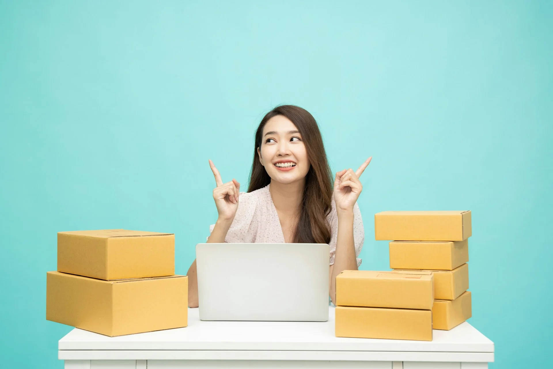 Perempuan pemilik toko online duduk di depan laptop di antara tumpukan kardus paket pesanan