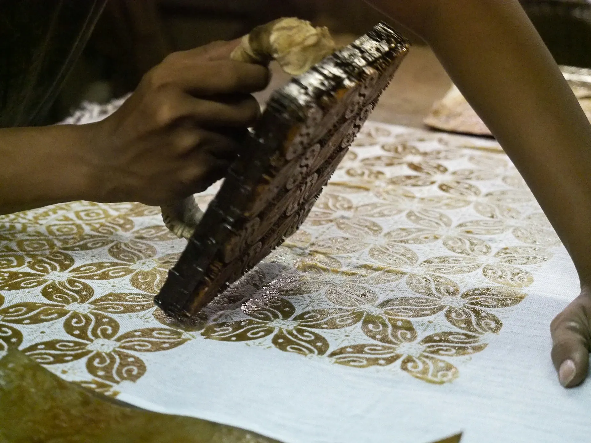 Tangan perajin menekan canting cap tembaga bermotif ke kain putih untuk membuat batik cap
