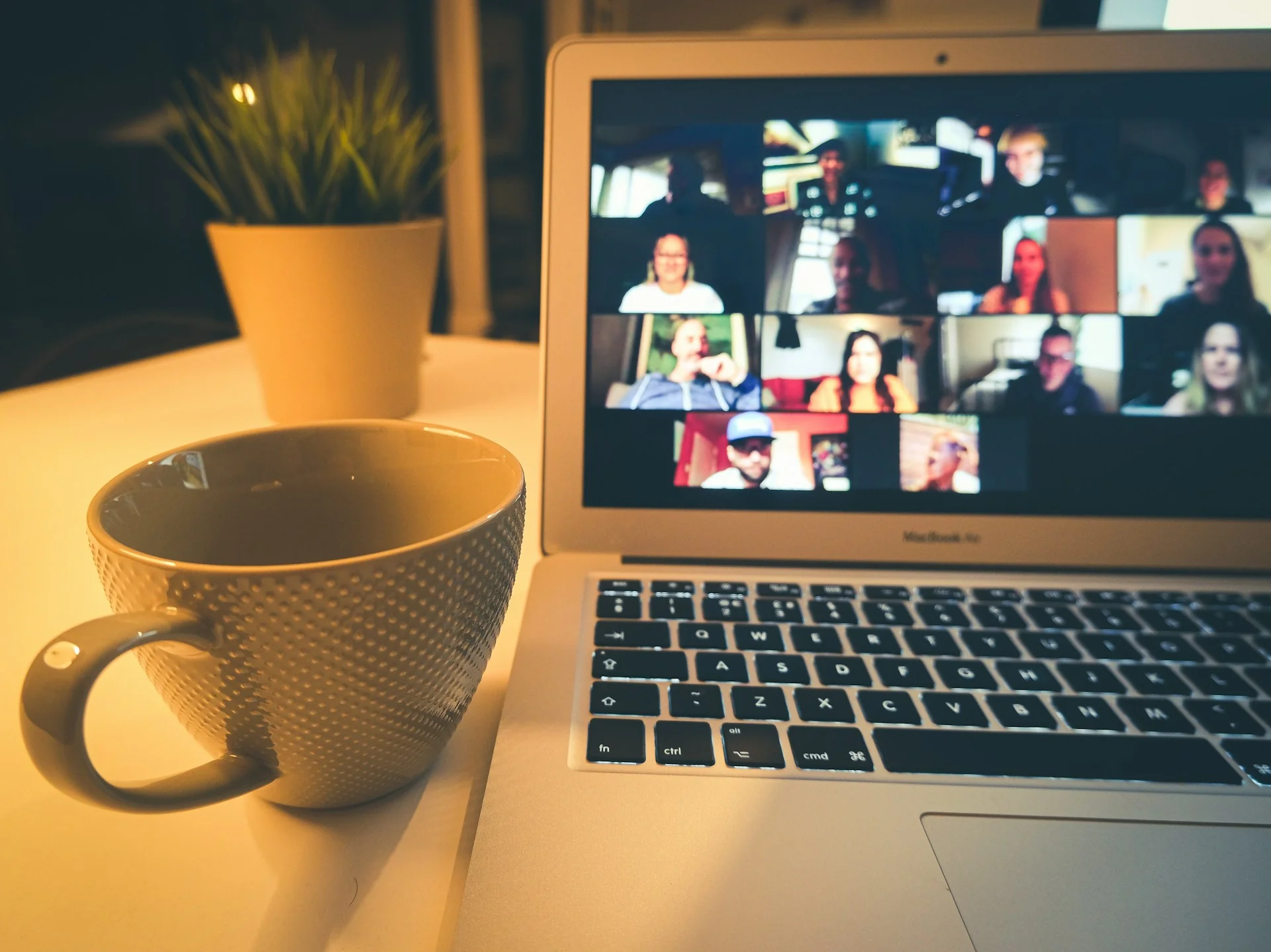 Laptop menampilkan rapat video dengan banyak peserta di samping cangkir kopi