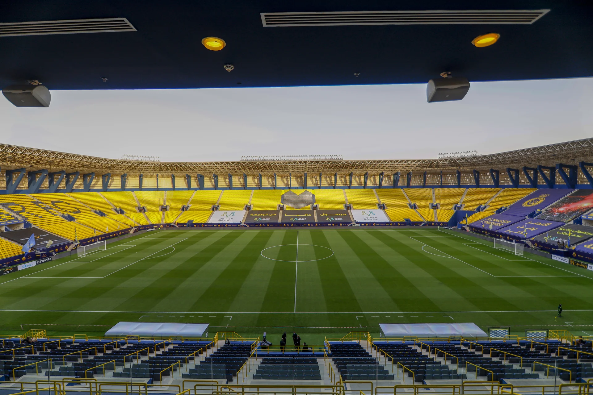 Interior Stadion King Saud University (Al-Awwal Park) di Riyadh dengan tribun kuning-biru dan lapangan kosong