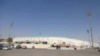Tampak luar Stadion Internasional Amman di Yordania dengan atap tribun putih, menara lampu, dan area parkir
