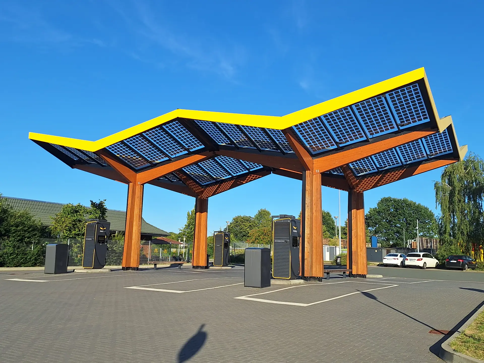 Deretan unit DC fast charger hitam di bawah kanopi panel surya stasiun pengisian umum